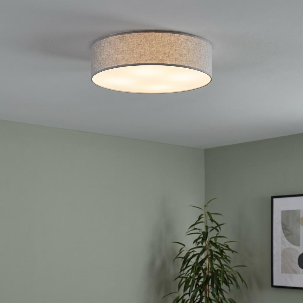 Flush mount ceiling light with a grey linen drum shade and warm glow in a room with soft green walls.