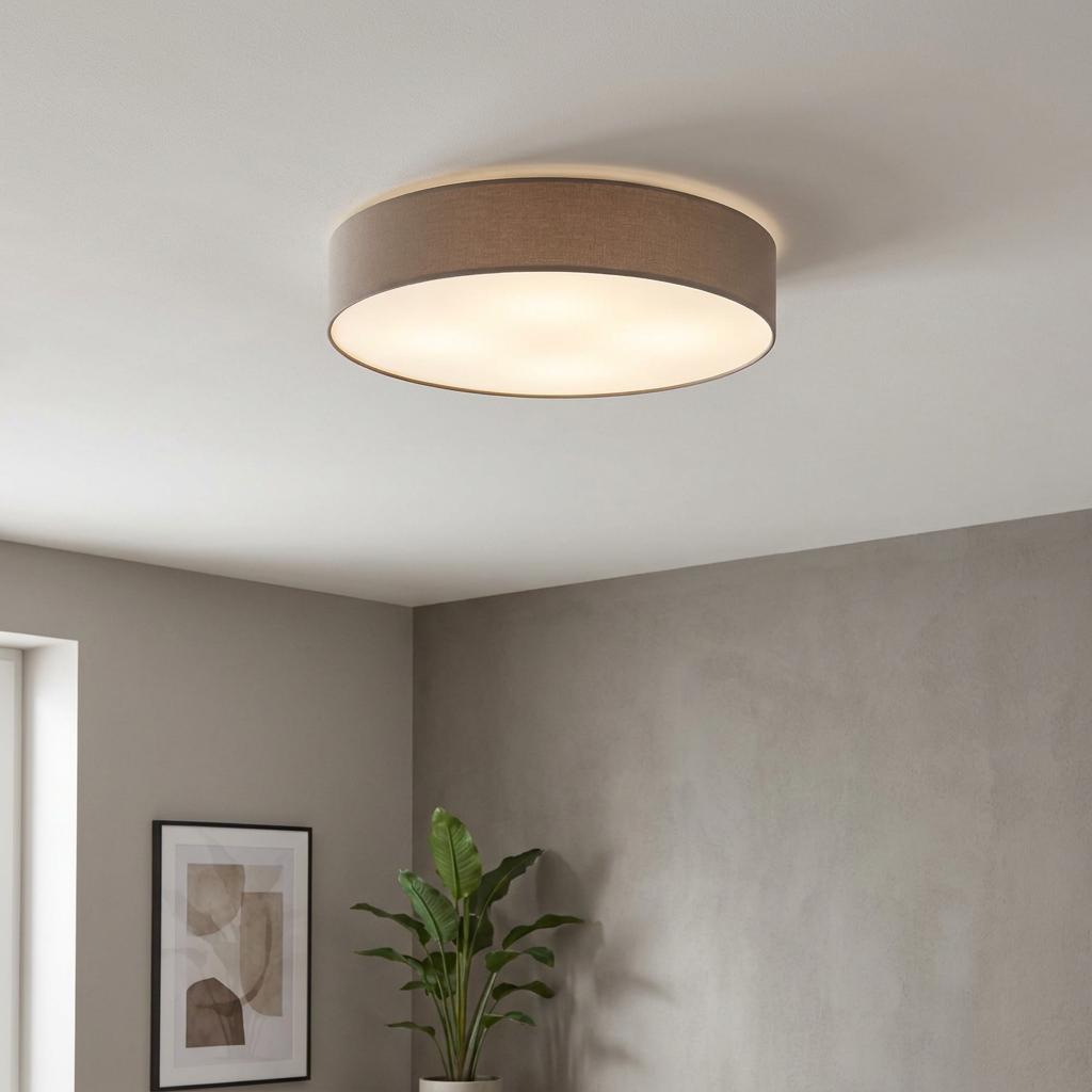 Taupe fabric drum flush ceiling light illuminating a modern room with grey walls and a green plant.