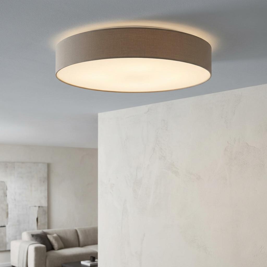 Large taupe fabric drum ceiling light with a white diffuser illuminated in a modern minimalist interior.