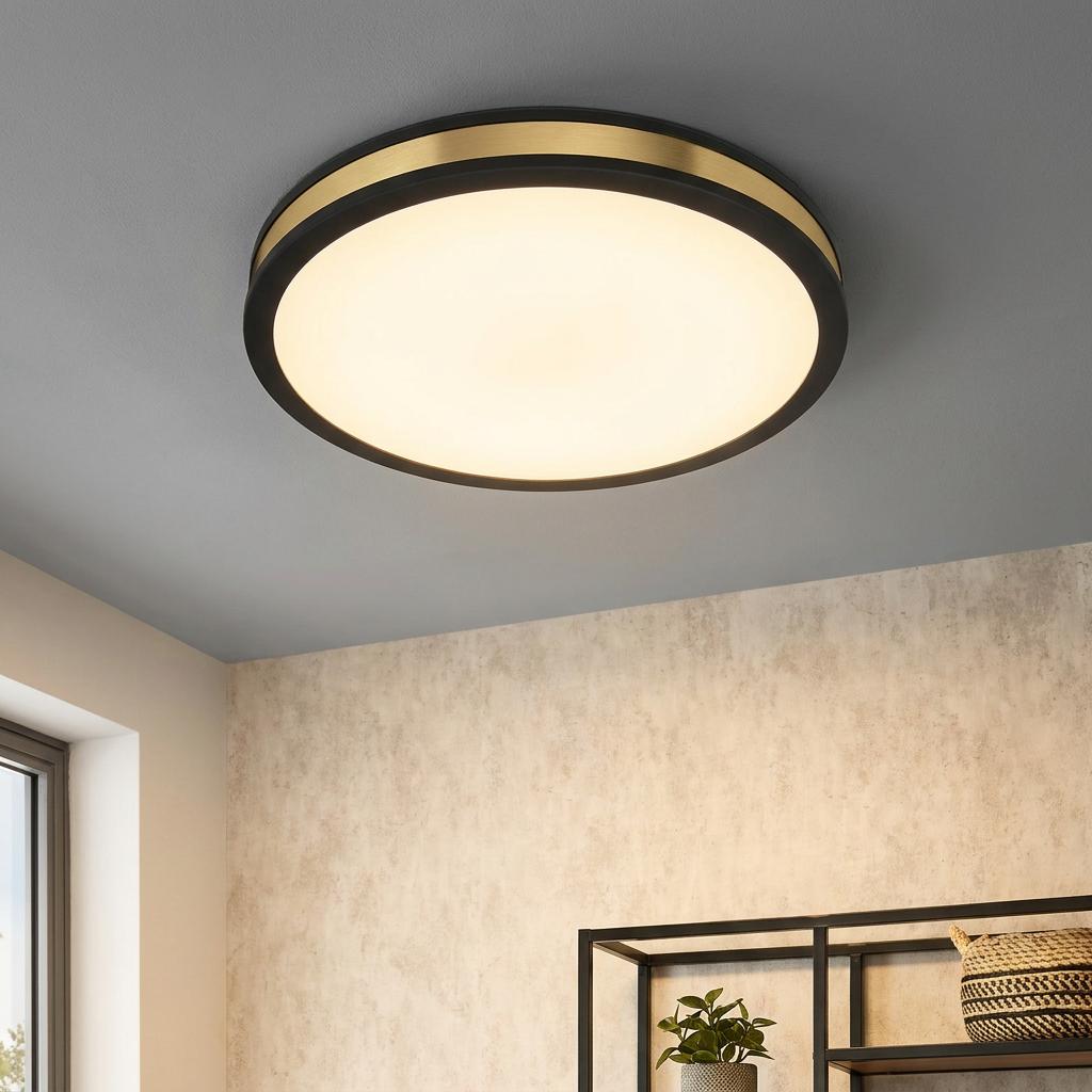 Round black and gold LED flush ceiling light illuminated on a grey ceiling.