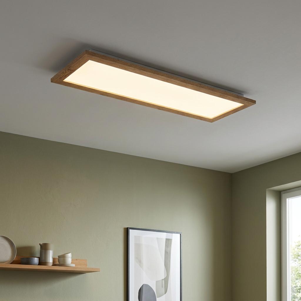 Rectangular wooden framed LED panel light glowing on a ceiling in a modern room with olive green walls.