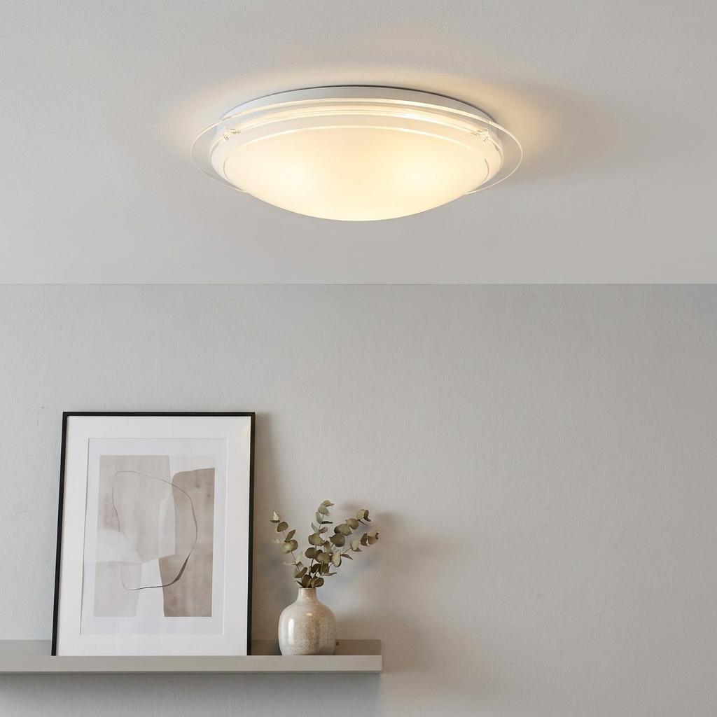Illuminated circular white painted glass flush ceiling light mounted on a white ceiling above a shelf.