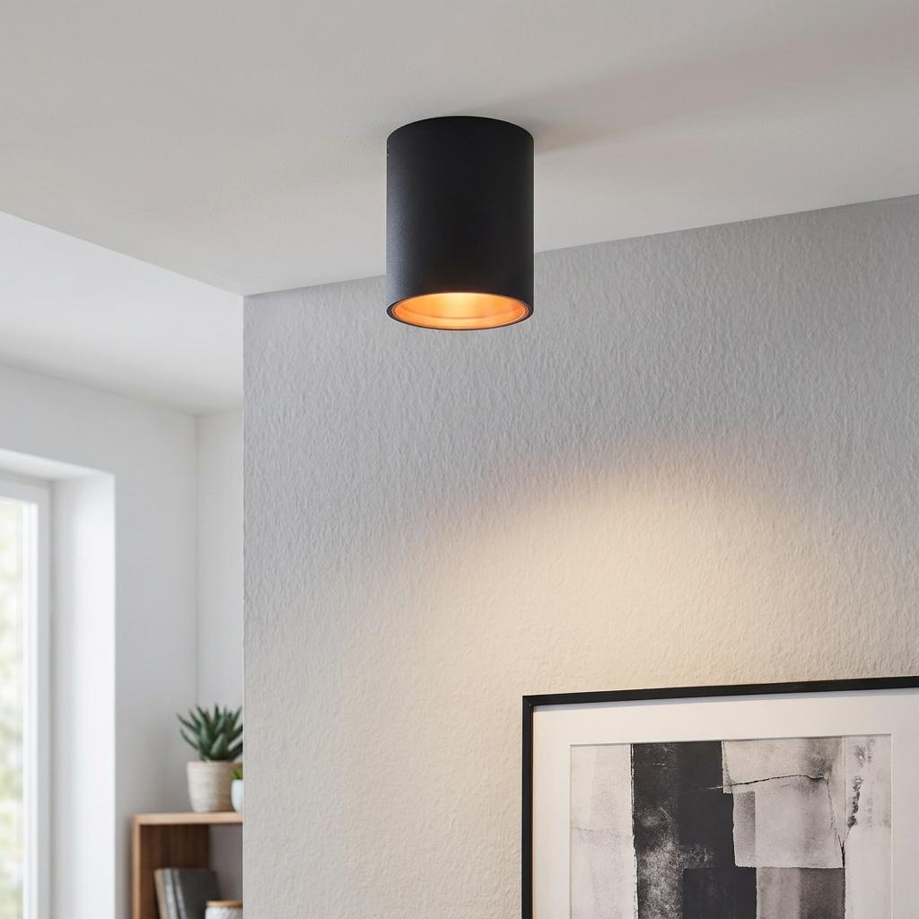Black cylindrical flush LED ceiling light with a warm copper interior glowing on a white ceiling.