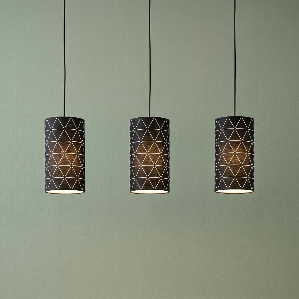 Three black cylindrical pendant lights with a geometric wireframe pattern hanging against a pale green wall.