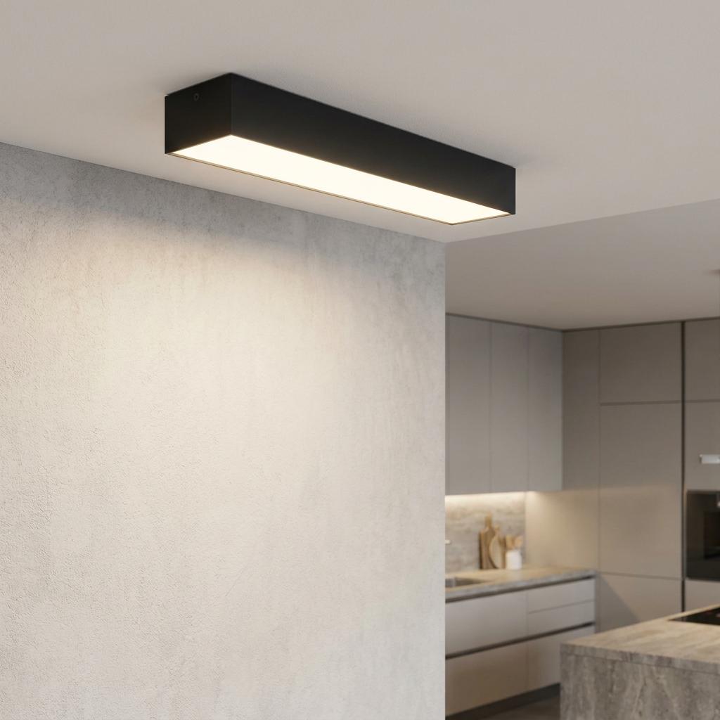 A black rectangular LED flush ceiling light illuminating a light grey wall in a modern kitchen setting.
