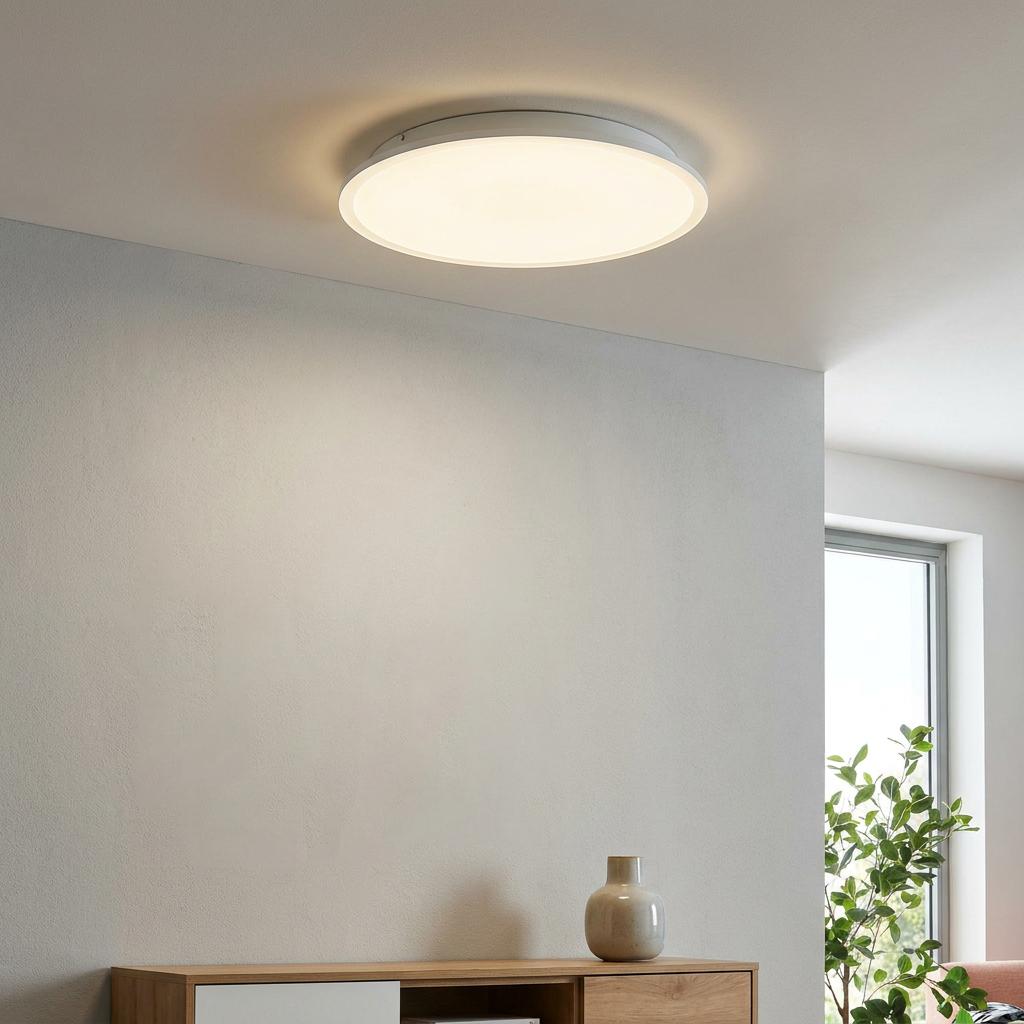 Slim circular white LED ceiling flush light glowing in a minimalist room with a wooden sideboard.