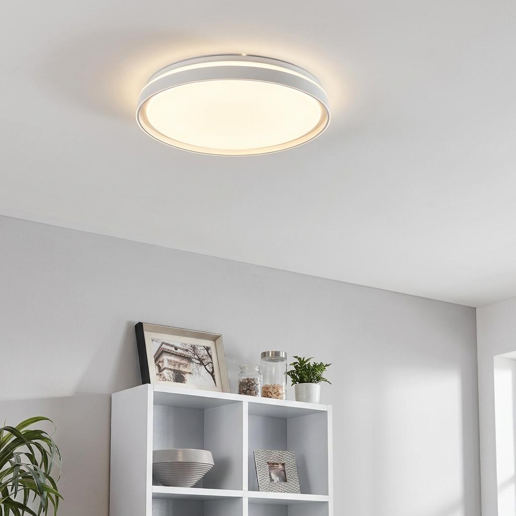 White circular LED flush ceiling light with a warm glow mounted in a modern living space above white shelves.