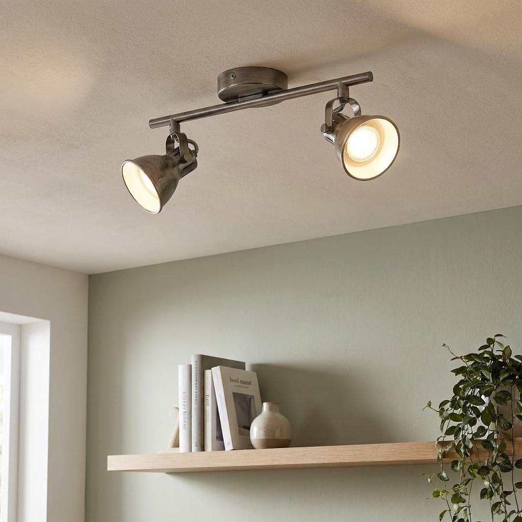 Antique nickel 2-light bar spotlight mounted on a ceiling above a wooden shelf in a modern interior.