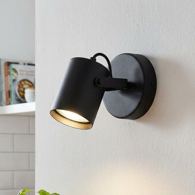 A black cylindrical wall spotlight illuminates a basil plant and bowl in a bright kitchen setting.