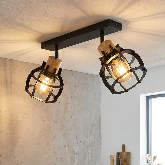 Industrial 2-light black and wood bar spotlight mounted over a dining table in a kitchen with concrete walls.