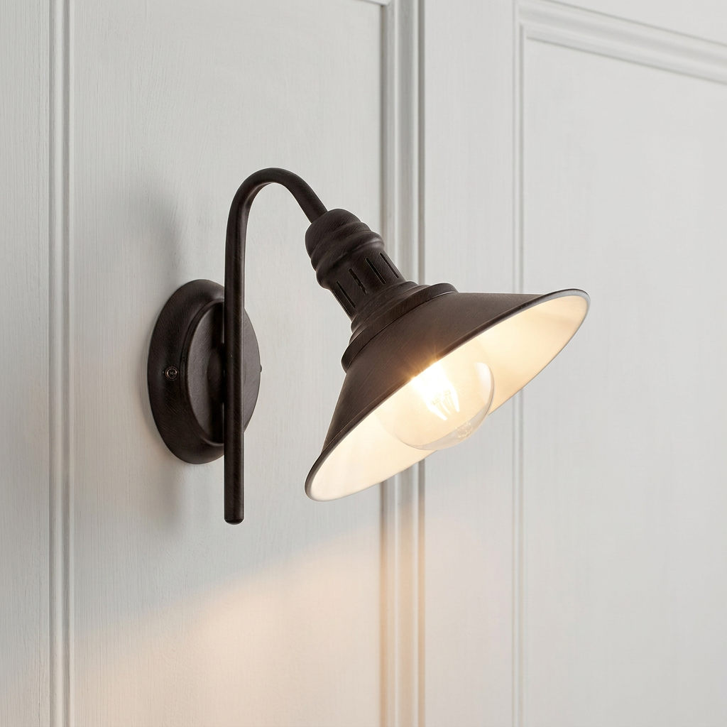 Antique brown wall light with a swan neck arm and metal cone shade, mounted and lit on a white paneled wall.
