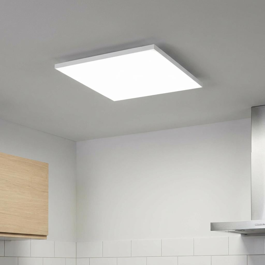 White square LED flush ceiling light illuminated in a modern kitchen with wood cabinets and subway tiles.