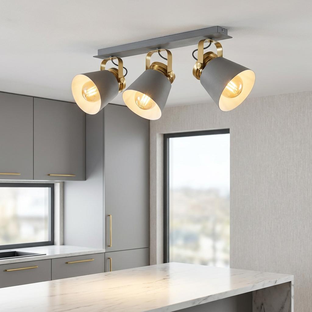 A grey and gold three-light bar spotlight fixture mounted on a kitchen ceiling over a marble island.