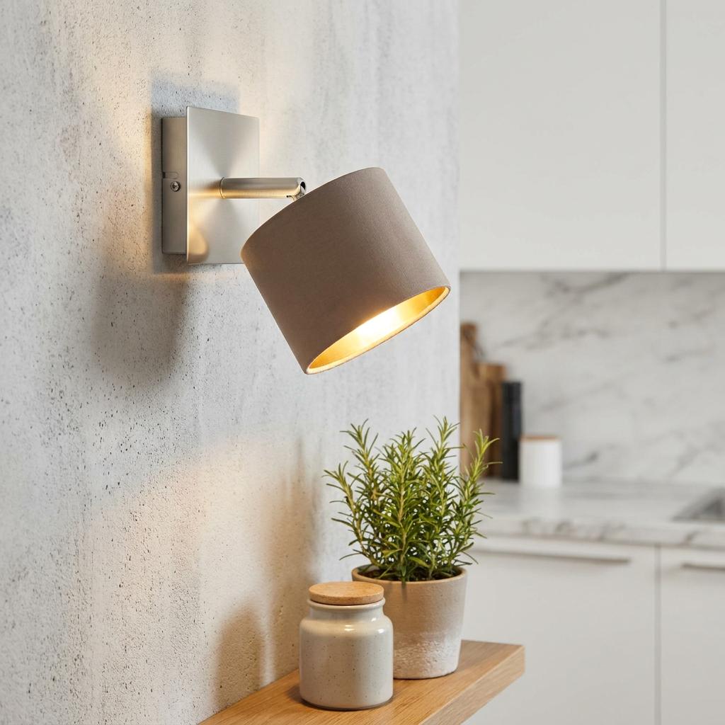Modern wall spotlight with a taupe fabric shade and gold interior, mounted on a textured wall above a wooden shelf.