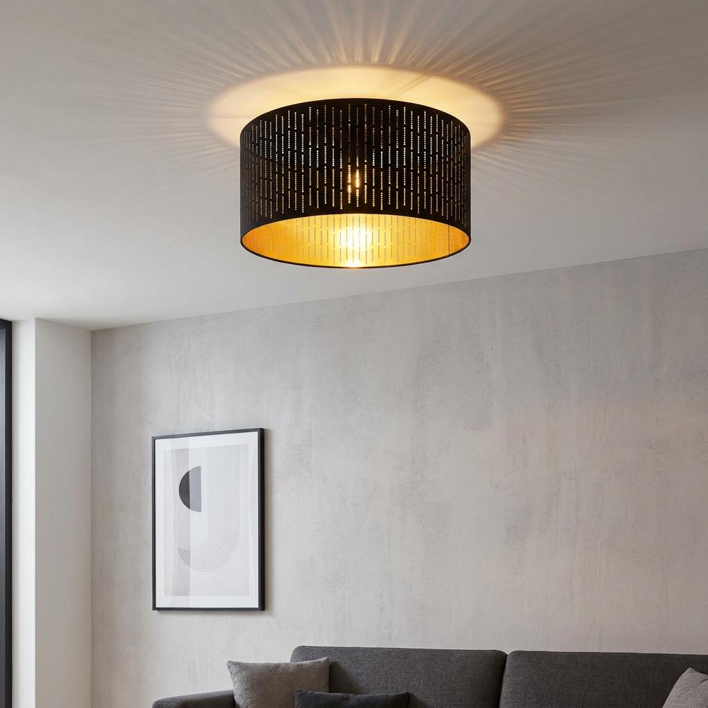 Black and gold flush ceiling light with dashed cutouts, casting radial light patterns in a modern living room.