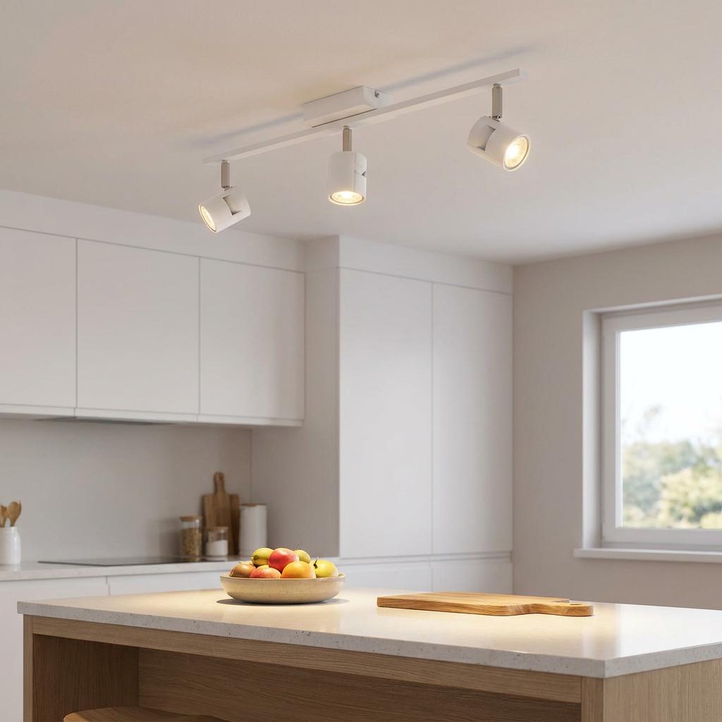 White three-light bar spotlight illuminating a bowl of fruit on a modern kitchen island.