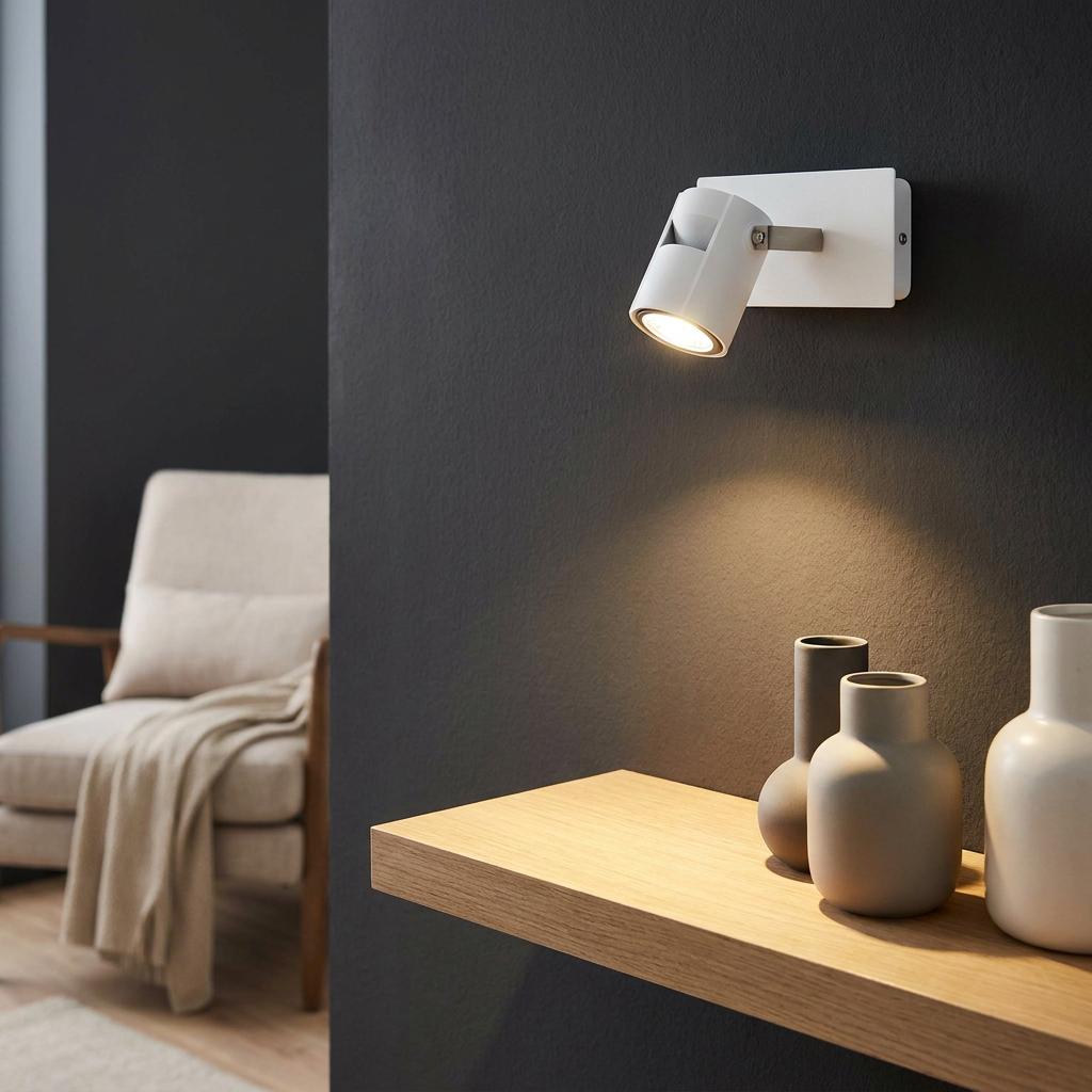 White Eglo Vergiano wall spotlight illuminating a wooden shelf with ceramic vases against a dark textured wall.