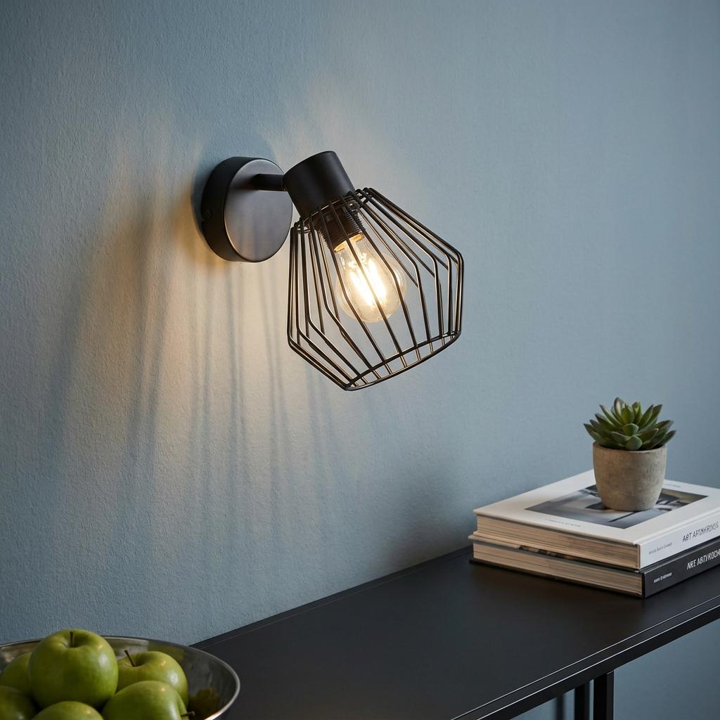 Black wire caged wall spotlight illuminated on a blue wall, casting geometric shadows above a black table.