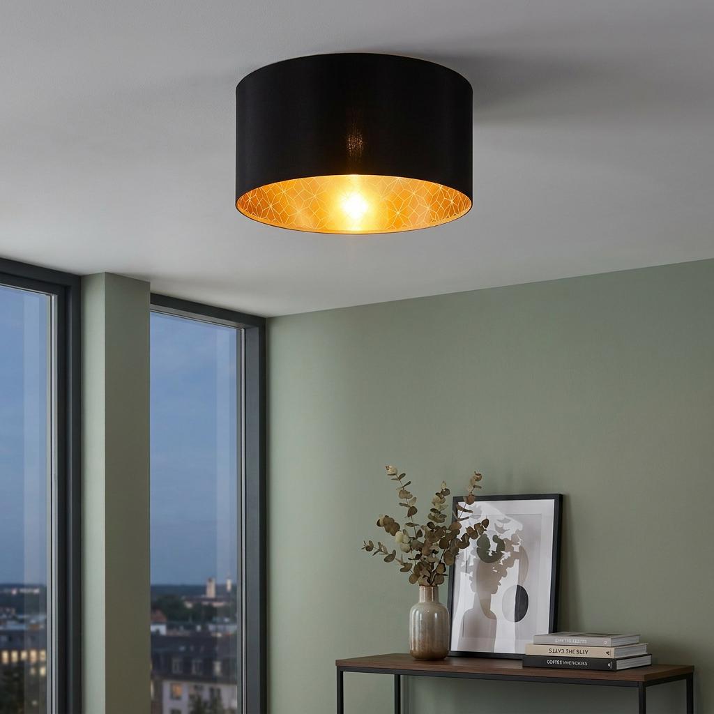 Black drum flush ceiling light with a glowing gold geometric interior, mounted in a modern living room.