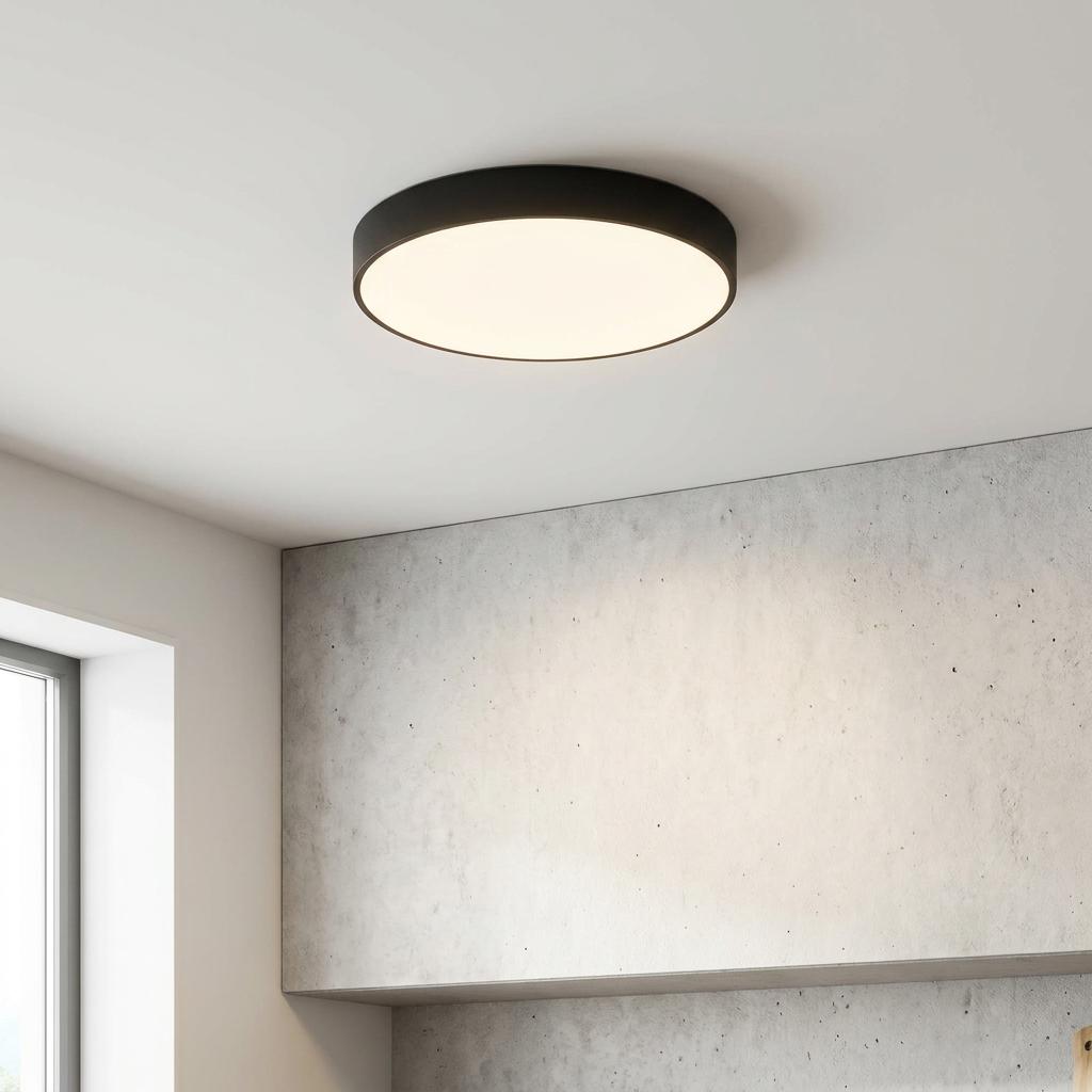 Modern black circular flush ceiling light mounted on a white ceiling above a textured grey wall.