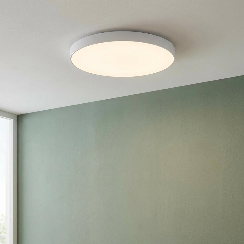 Round white flush LED ceiling light illuminating a room with a soft glow above a light green wall.
