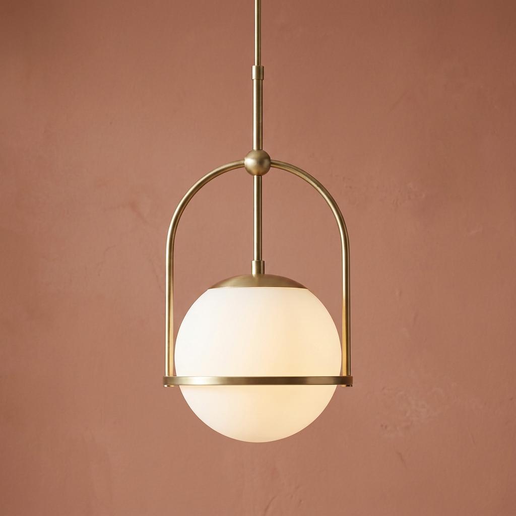 Art Deco pendant light featuring a brass hoop frame and opal glass globe shade, set against a terracotta wall.
