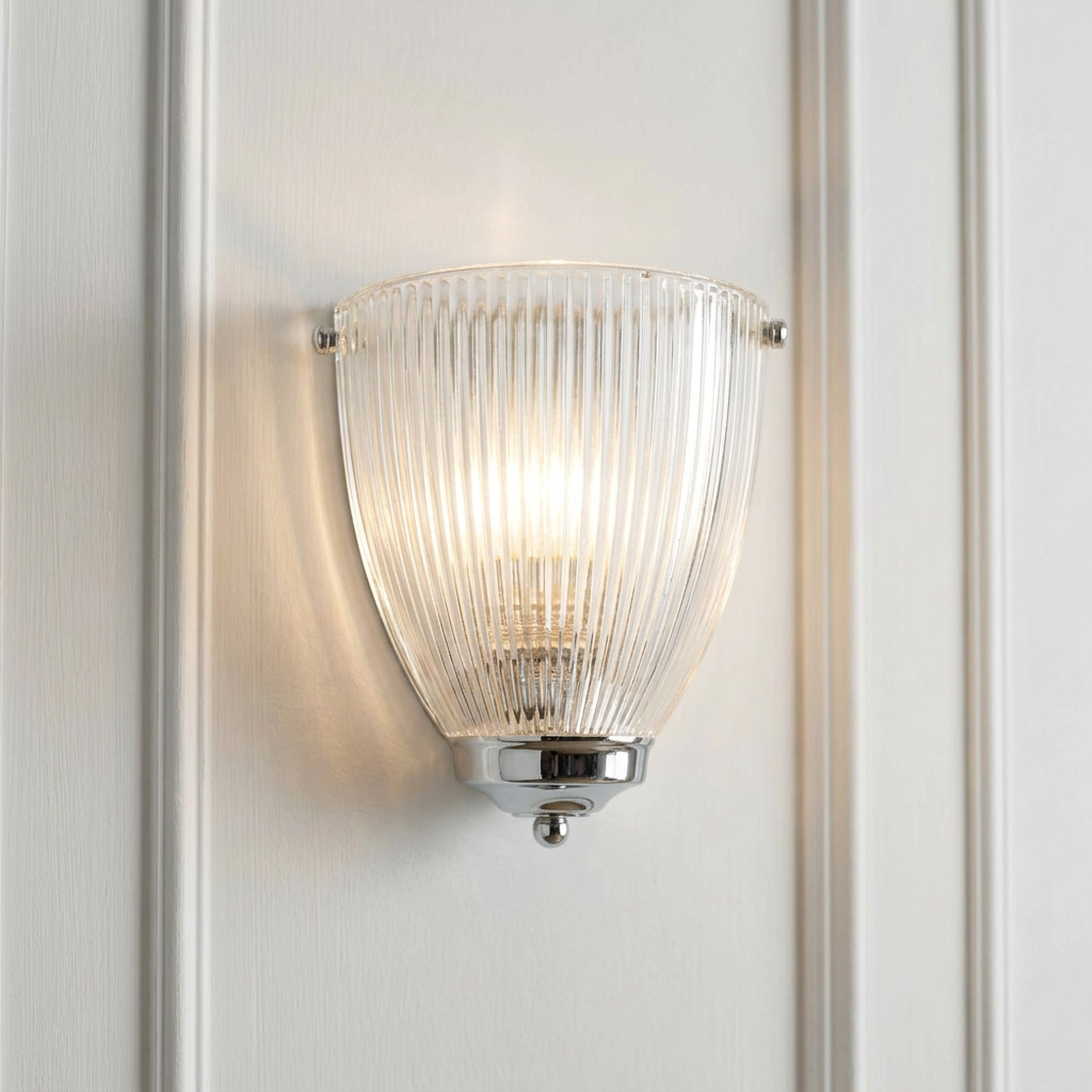 Elongated prismatic glass wall light with a chrome base, illuminated against a white paneled wall.