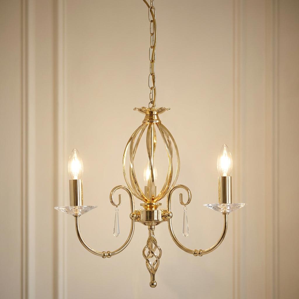 Elstead Aegean polished brass 3-light chandelier with crystal accents and glowing candle bulbs against a paneled wall.