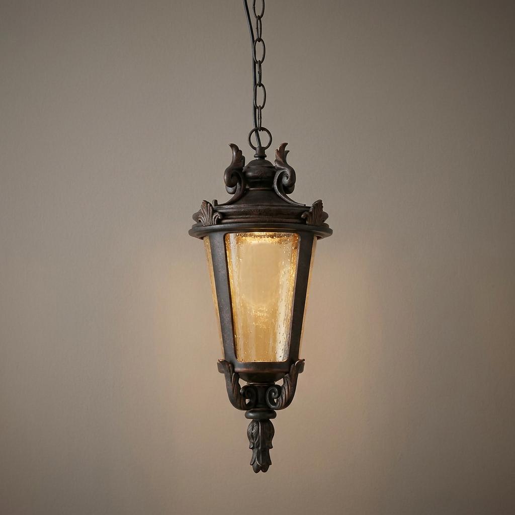 Lit weathered bronze outdoor hanging lantern with seeded amber glass suspended by a chain.
