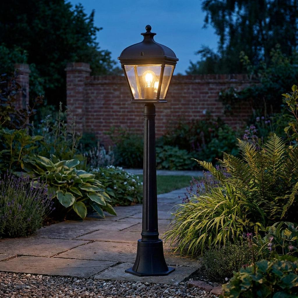 Elstead Bayview black medium outdoor bollard light illuminating a stone garden path at dusk.
