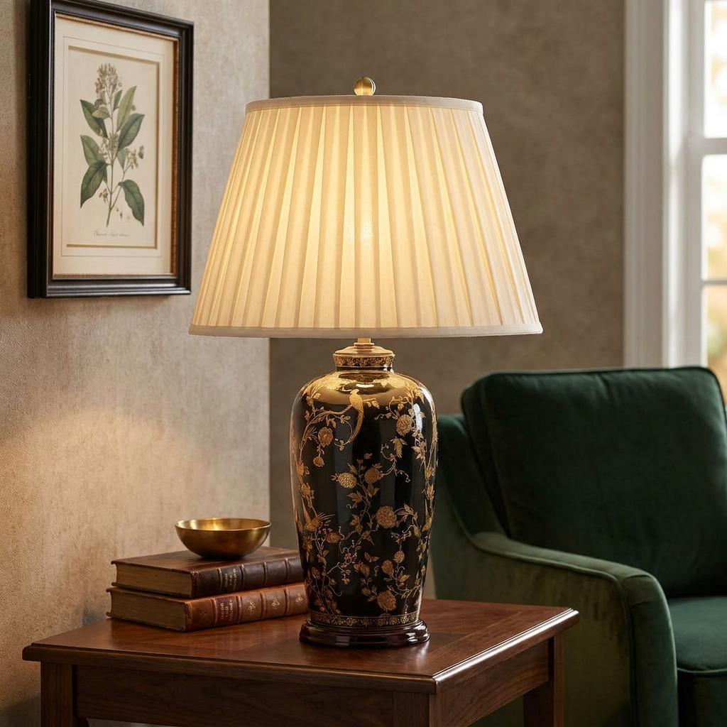 Elstead black and gold bird patterned ceramic table lamp with a pleated cream shade on a wooden side table.