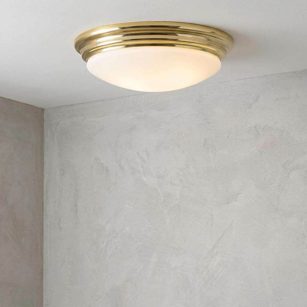 Polished brass bathroom flush mount light with a frosted white glass dome installed on a white ceiling.