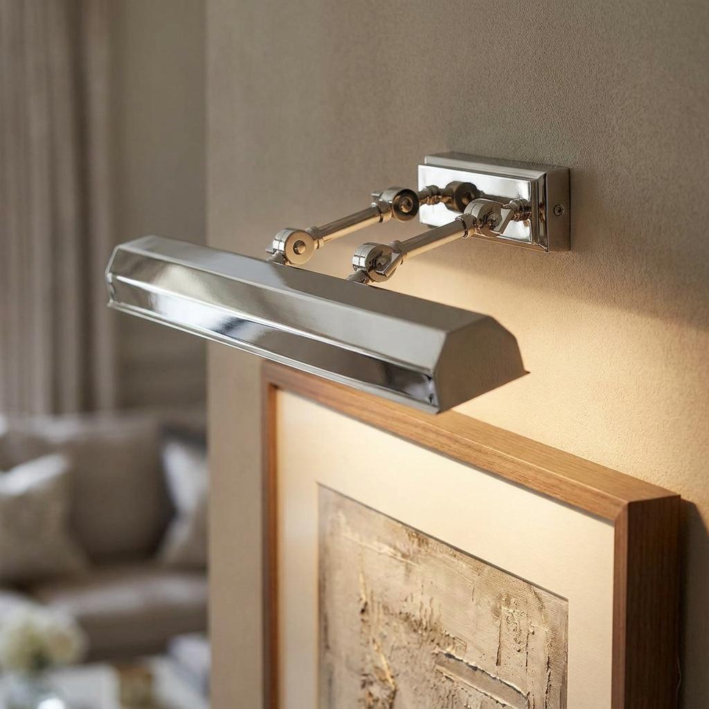 Polished nickel picture light with adjustable arms mounted on a wall, illuminating a framed artwork below.