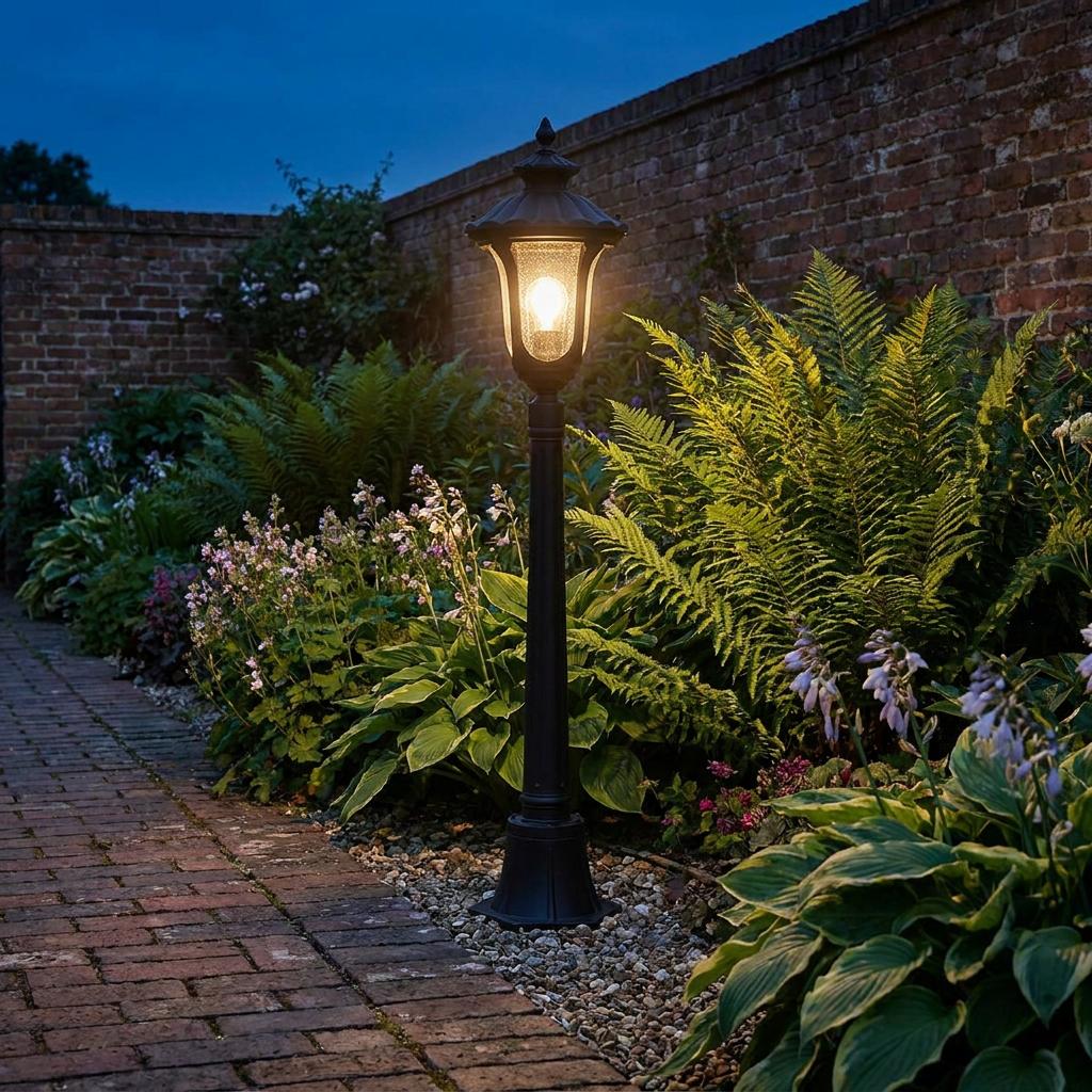 Traditional black bollard lantern with warm seeded glass illuminating a lush garden path at twilight.