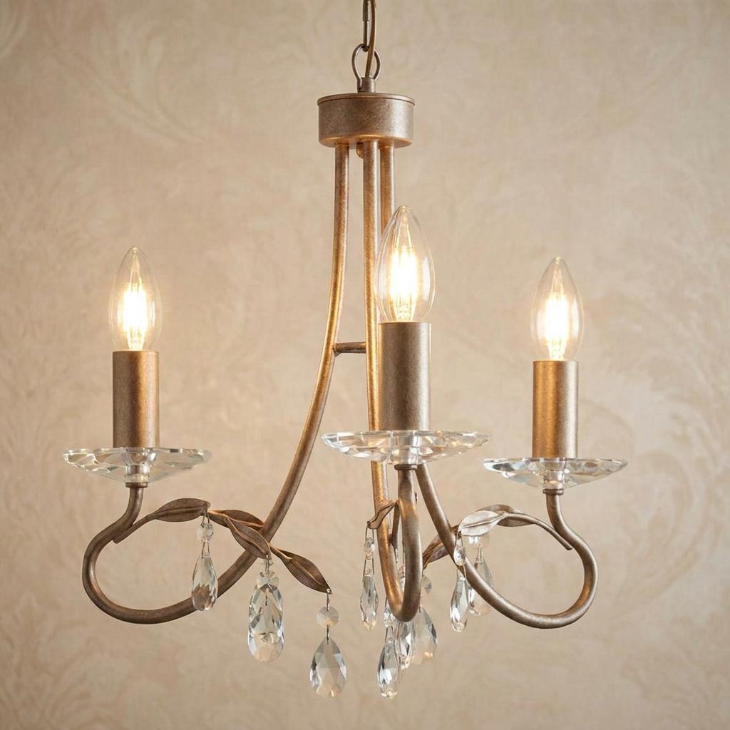 Three-light chandelier in silver and gold with leaf details and crystal droplets, hanging against patterned wallpaper.