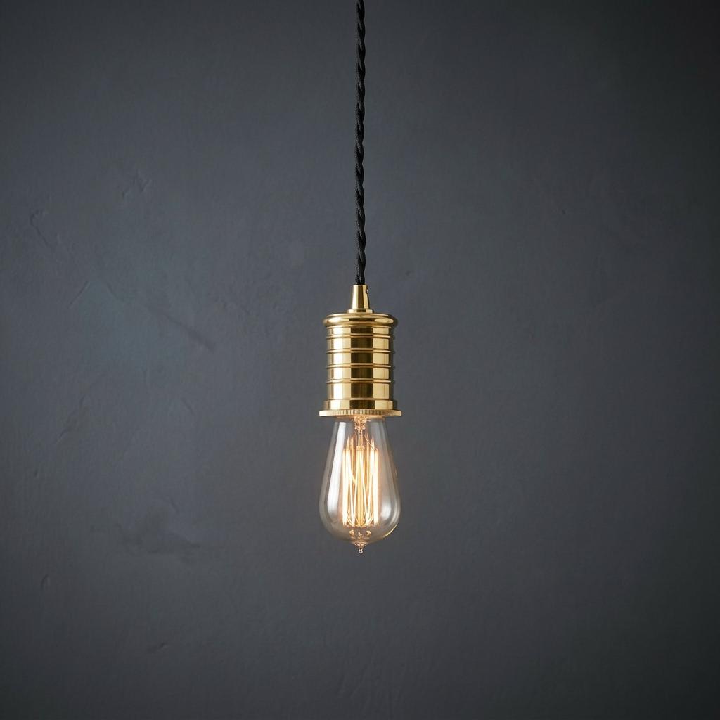 Polished brass pendant light with a vintage Edison bulb hanging against a dark grey textured wall.