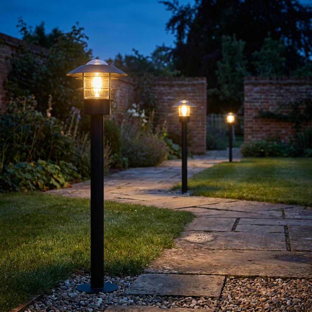 Three black bollard lights with tiered tops illuminating a stone garden path at dusk.