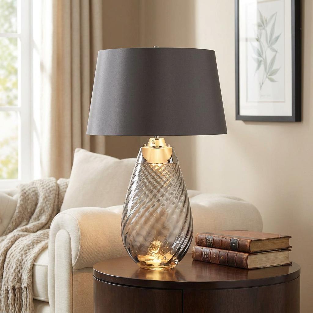 Elstead Lena 2 Light Large Smoke Glass Table Lamp with a charcoal drum shade on a wooden table in a living room.