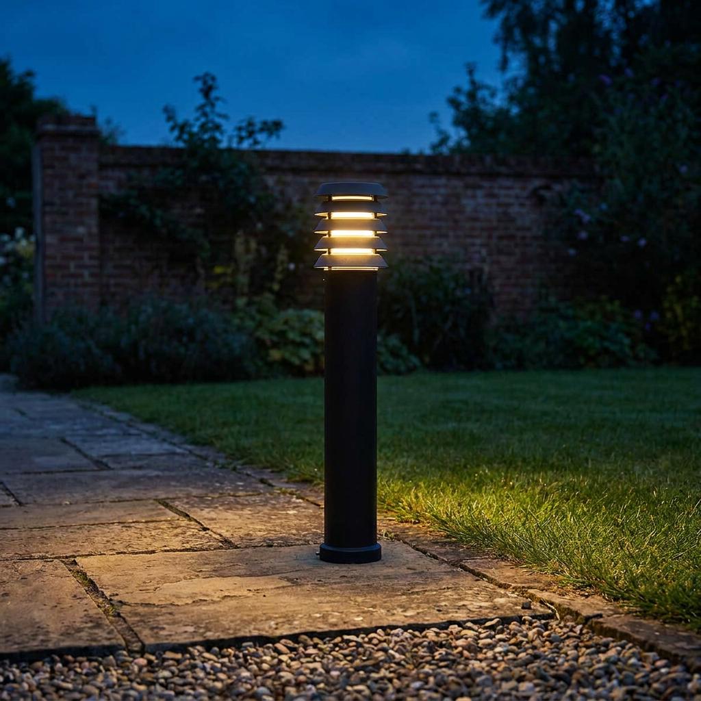 An Elstead Lighting Alta black bollard light illuminating a stone path in a garden at dusk.
