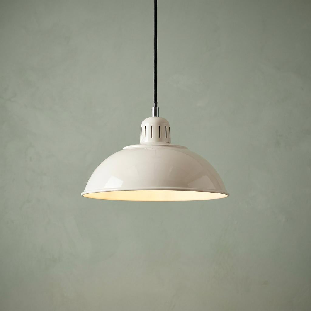 A cream dome-shaded pendant light with a black cord hanging against a pale green textured wall.