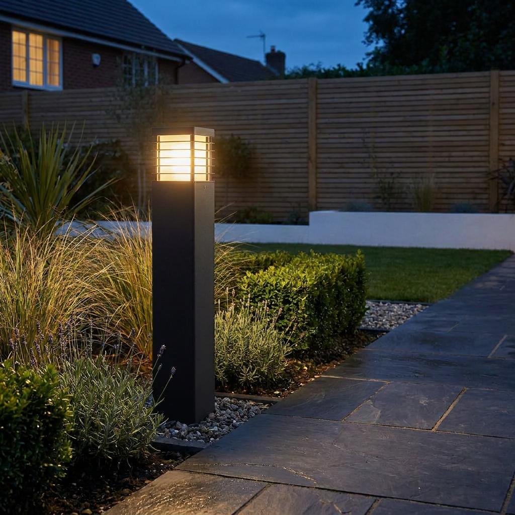 Black bollard light with horizontal slats glowing beside a garden path at twilight.