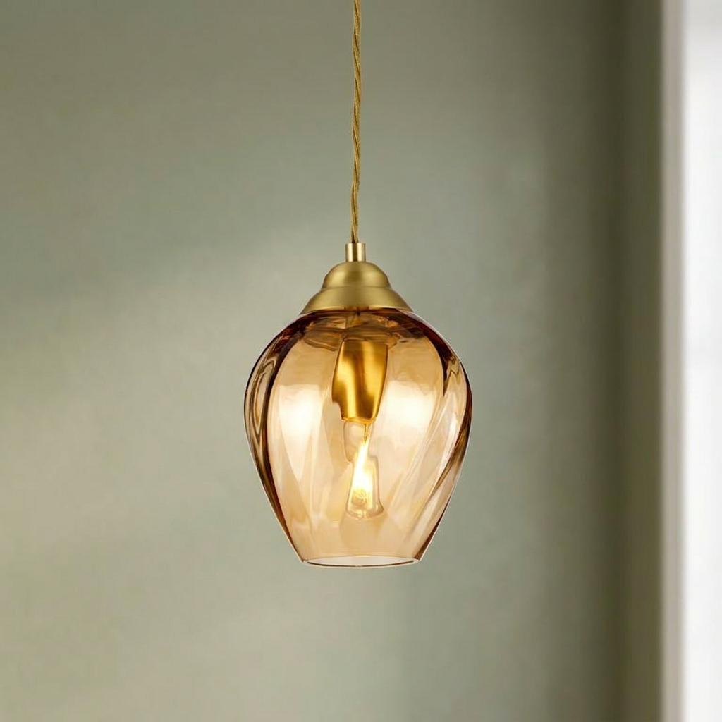 Amber swirl glass teardrop pendant light with brass fittings and a glowing bulb against a muted green wall.
