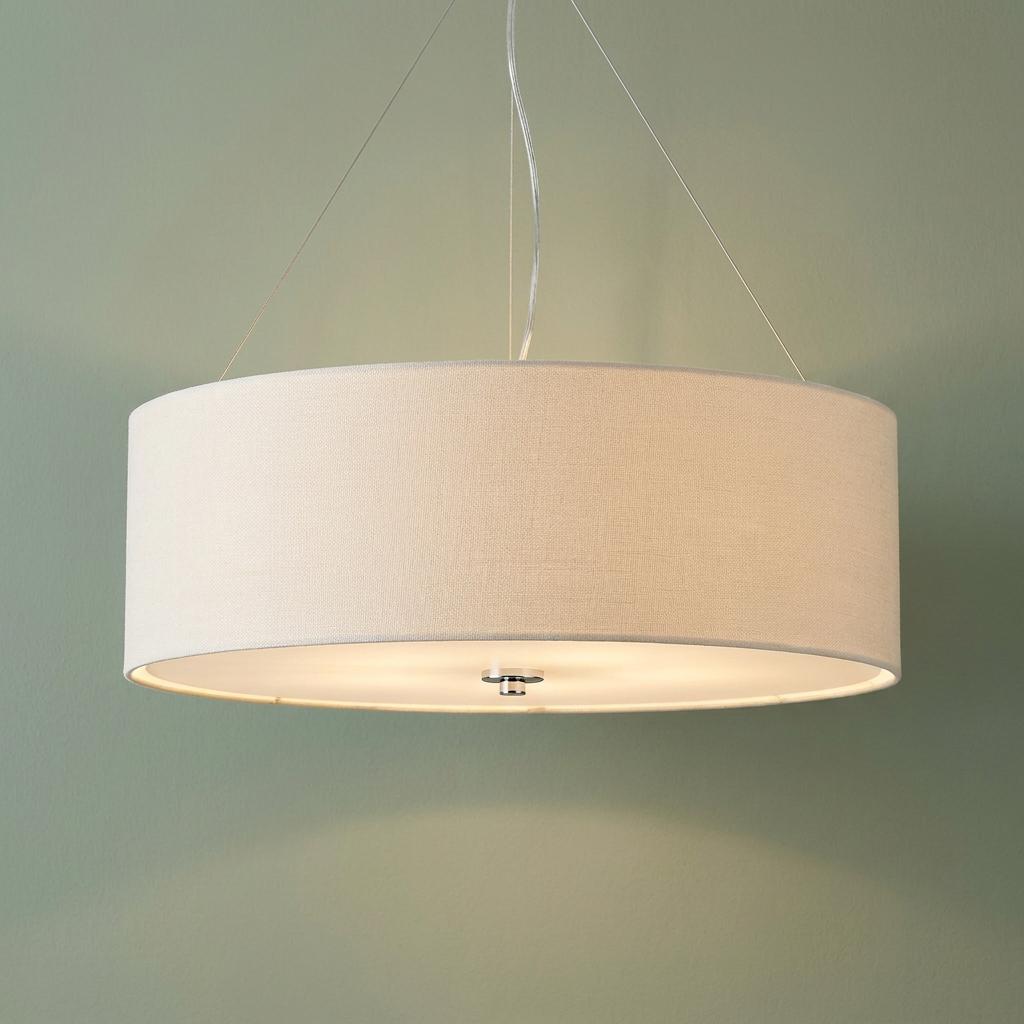 Large cream drum pendant light with a fabric shade suspended by thin wires against a muted green wall.
