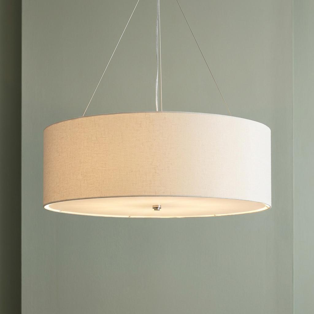 Large drum-shaped pendant light with a light-colored linen shade suspended from wires against a muted green wall.