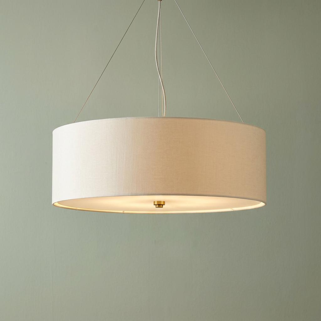 Large cream fabric drum pendant light with a central brass finial, suspended against a light green wall.