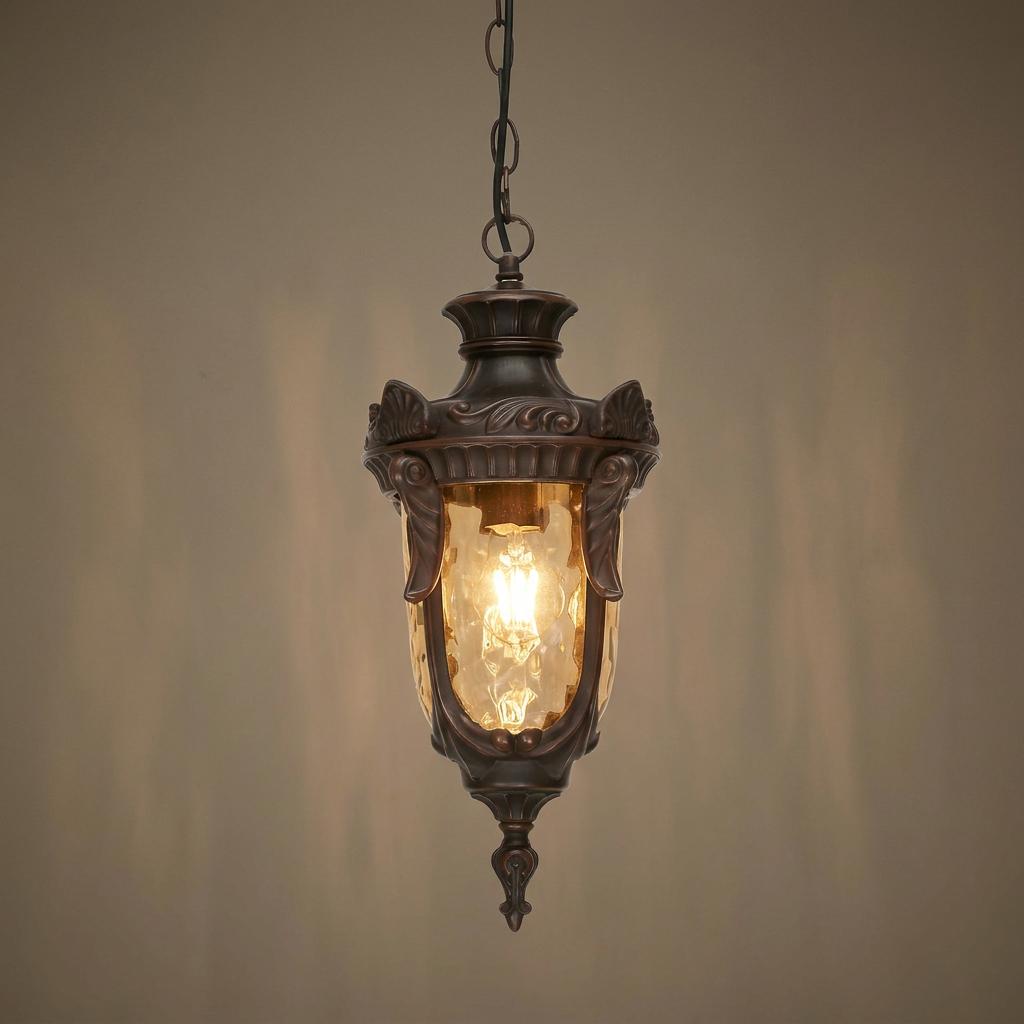 Bronze outdoor pendant light with amber glass and ornate detailing hanging against a textured wall.