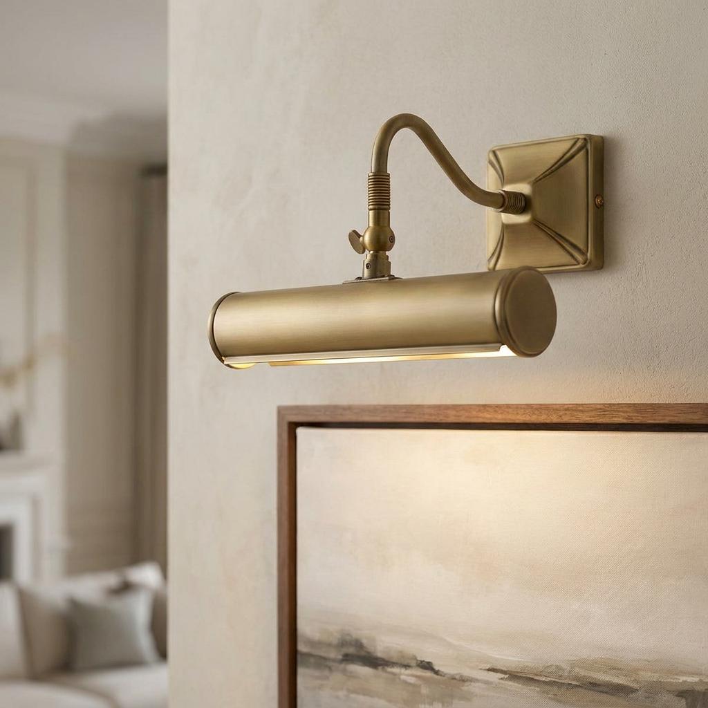A brushed brass picture light mounted on a wall, illuminating a framed landscape painting.