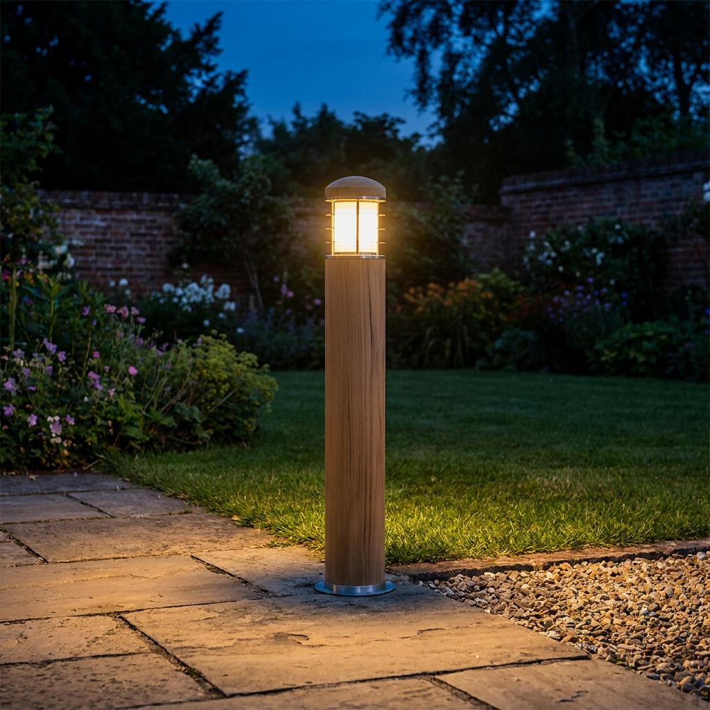 An Elstead Poole bollard light with a teak body and stainless steel cap illuminating a stone garden path at dusk.
