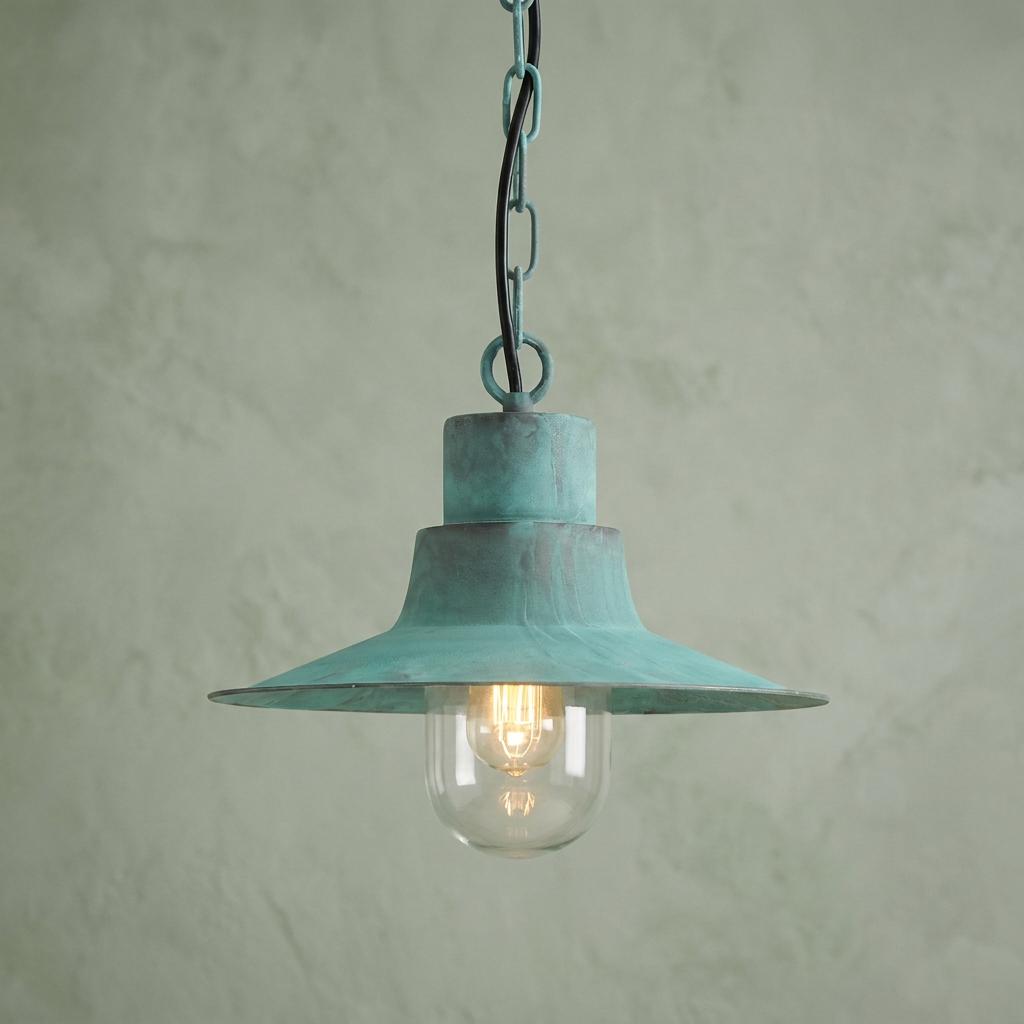 Verdigris outdoor pendant light with a wide metal shade and glass globe hanging against a textured wall.