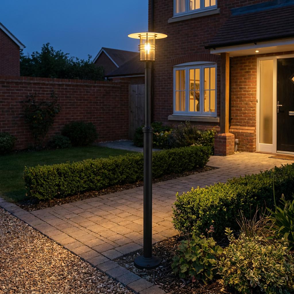 An Elstead Stockholm large black outdoor lamp post illuminates a brick path and garden at dusk.